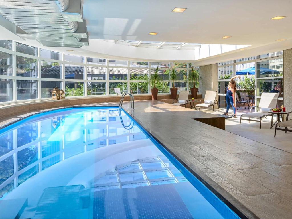 a large swimming pool in a hotel lobby with a woman walking in the background at Mercure Sao Paulo Jardins in Sao Paulo