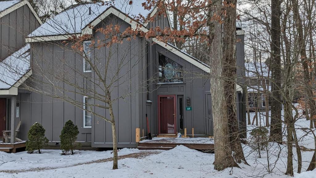 a gray house with a red door in the snow at Frost Hollow by AvantStay Deck w Grill Game Room Loft in White Haven