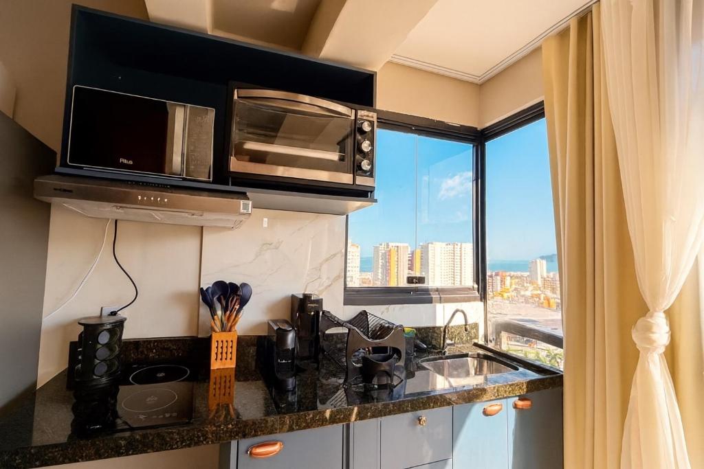 a kitchen with a counter with a microwave and a window at Lindo Studio a 600m da praia in Guarujá