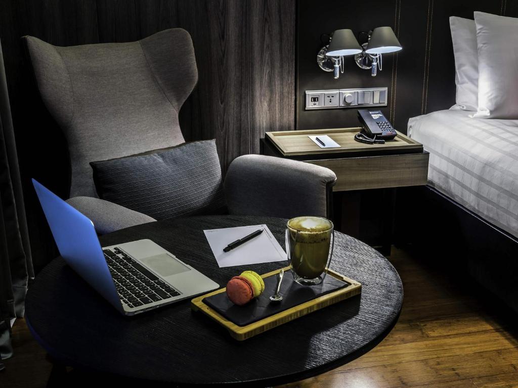 A compact in-room workspace with a laptop, round table, chair and bedside controls.