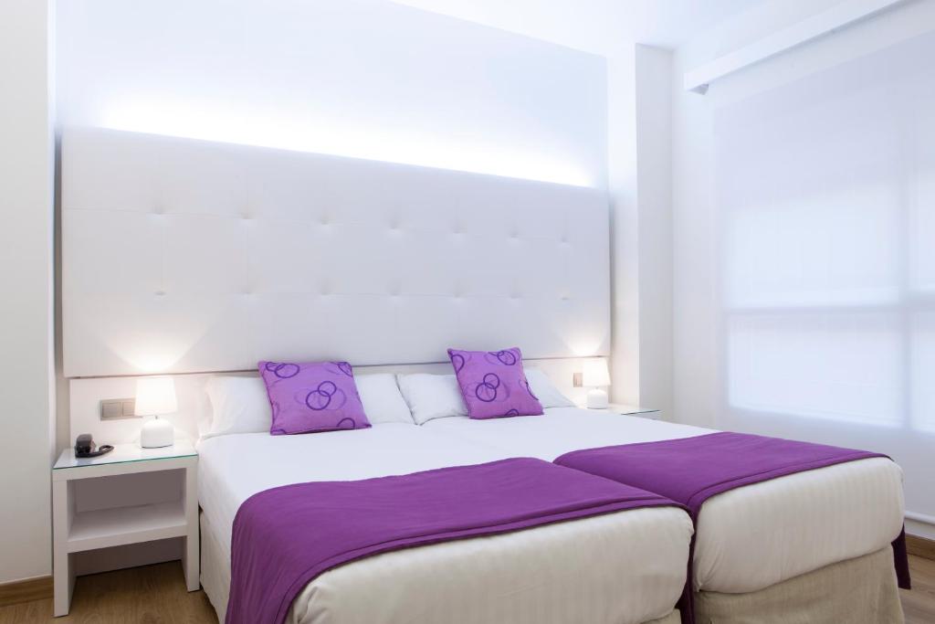 ein Schlafzimmer mit einem großen weißen Bett mit lila Kissen in der Unterkunft Hotel Albahia Alicante in Alicante