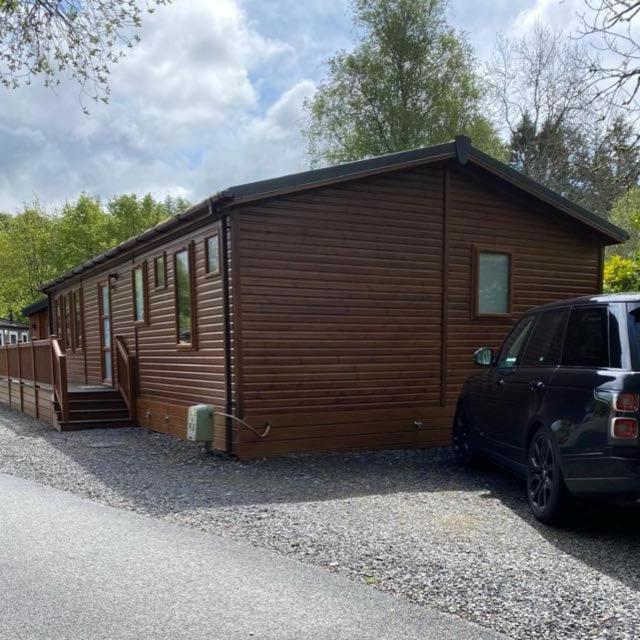a wooden cabin with a car parked in front of it at Hot Tub Lake District Lodge - Windermere in Troutbeck Bridge