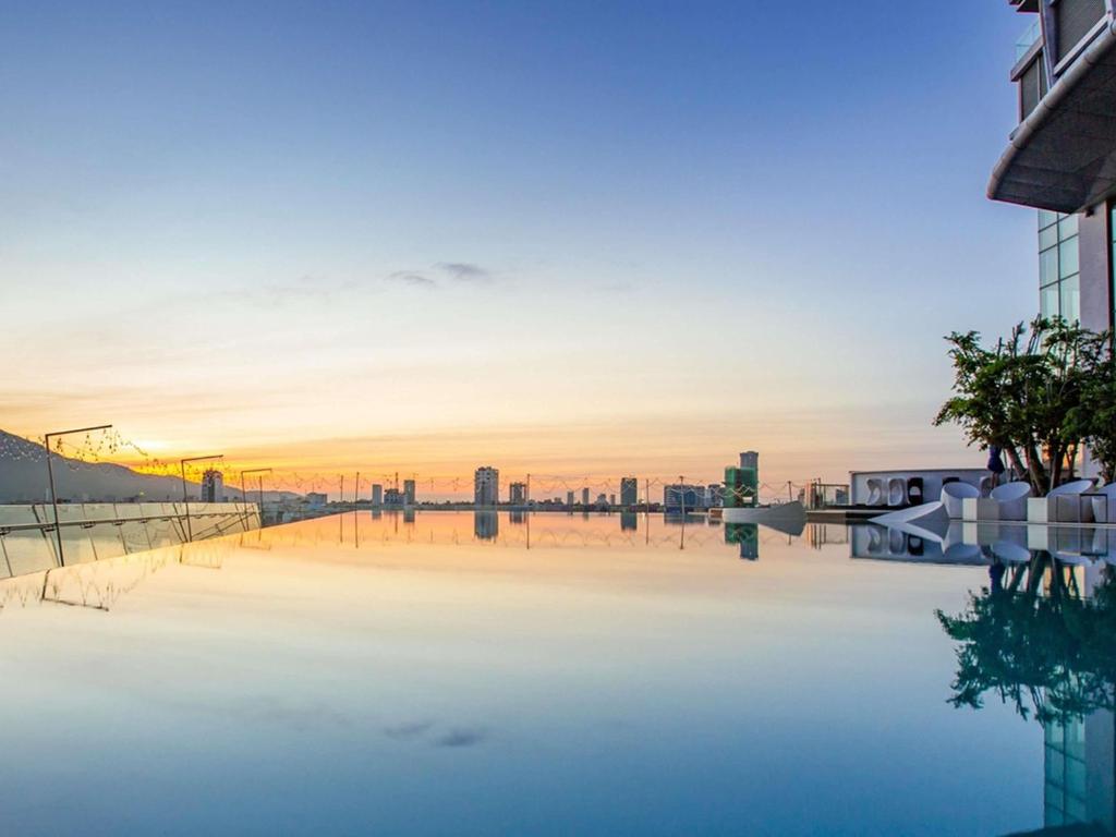 An infinity pool reflecting a pastel sunset and a distant city skyline.