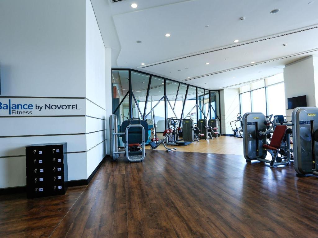 A bright fitness room with cardio and resistance machines beside full-height windows.
