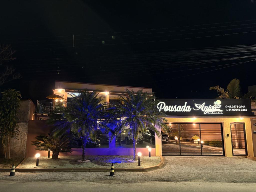 a building with palm trees in front of it at night at Pousada Anjos - à 2 quadras do mar in Matinhos