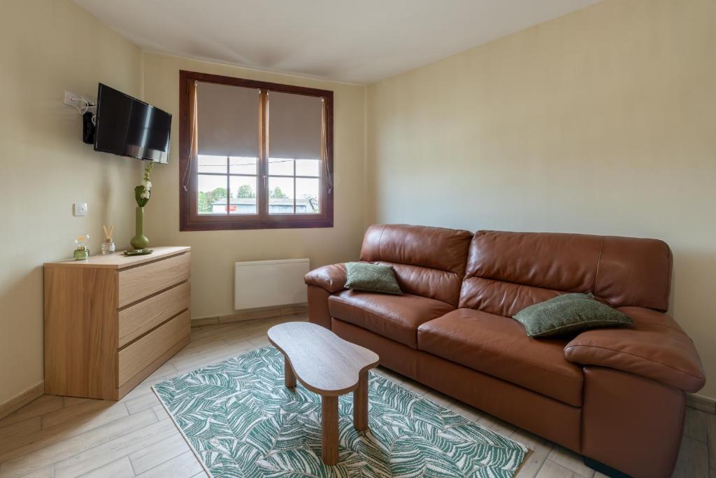 a living room with a brown leather couch and a stool at Le Reflet de Valéry - Proche Plage in Le Bois de Cise