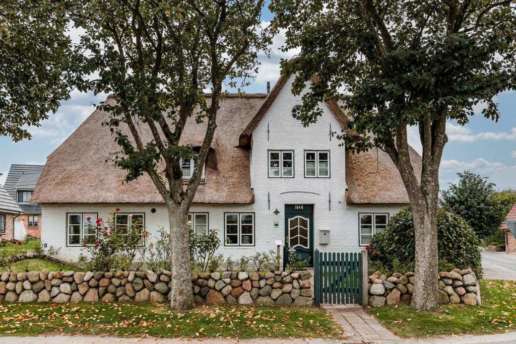 a white house with a stone wall and trees at Altes Schulmeisterhaus Wohnung 2 in Oevenum