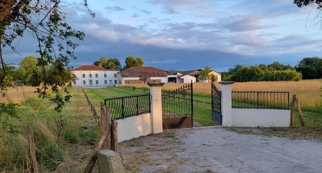 a gate to a white house in a field at Chalet en bois in Labatut