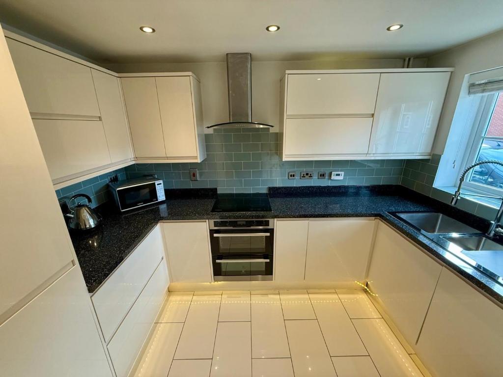 a kitchen with white cabinets and black counter tops at Knoll House - 6 separate beds in Bedford