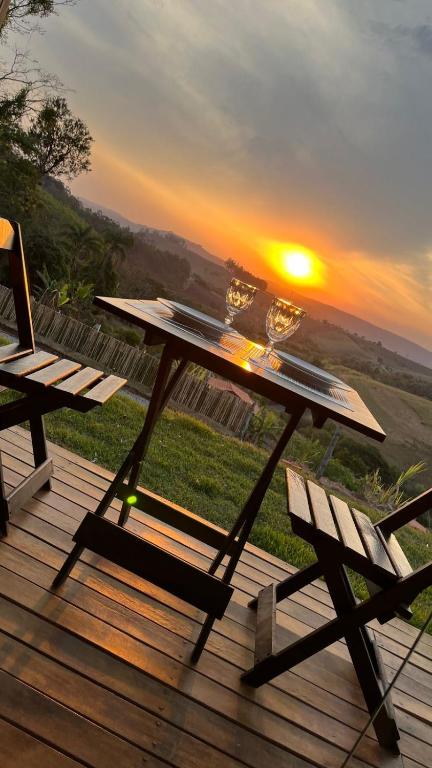 a picnic table and a bench on a deck with the sunset at Pousada Chalé privativa mirante do sol in Socorro
