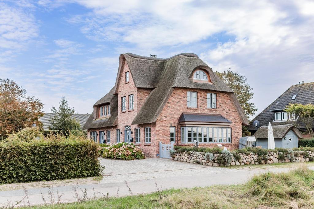 ein großes Backsteinhaus mit Reetdach in der Unterkunft Lottas Hüs in Borgsum