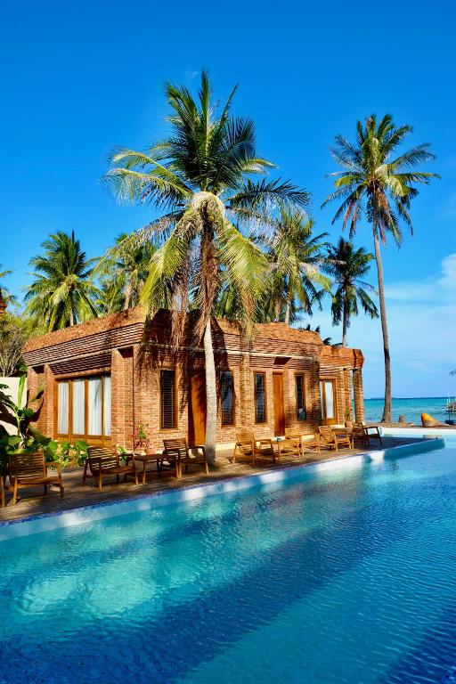 a swimming pool in front of a house with palm trees at Pulojava Resort in Karimunjawa