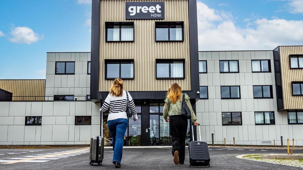 two women walking in front of a building with luggage at greet Hotel Reims Tinqueux in Reims