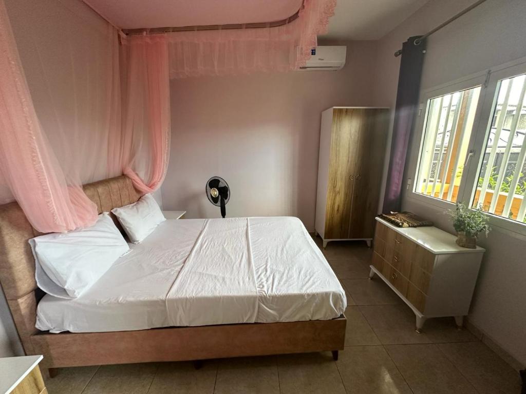 a bedroom with a bed with white sheets and pink curtains at Océan Voyages Mitsamihouli in Mitsamiouli