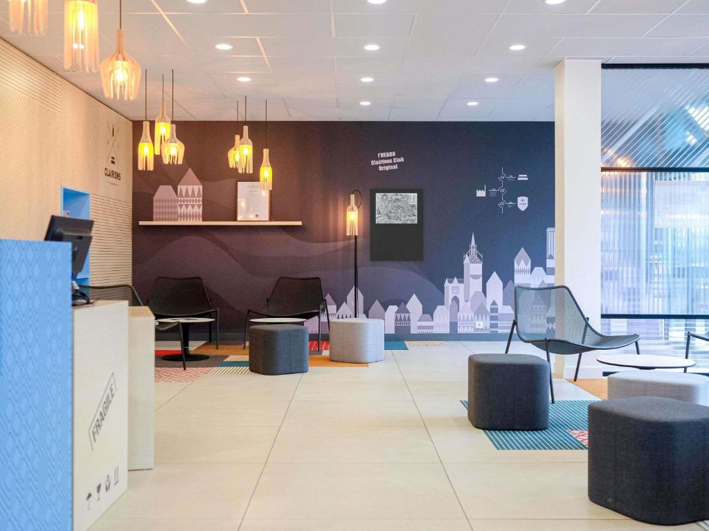 Un vestíbulo con sillas y mesas en un edificio. en Hôtel ibis Styles Auxerre Nord, en Auxerre