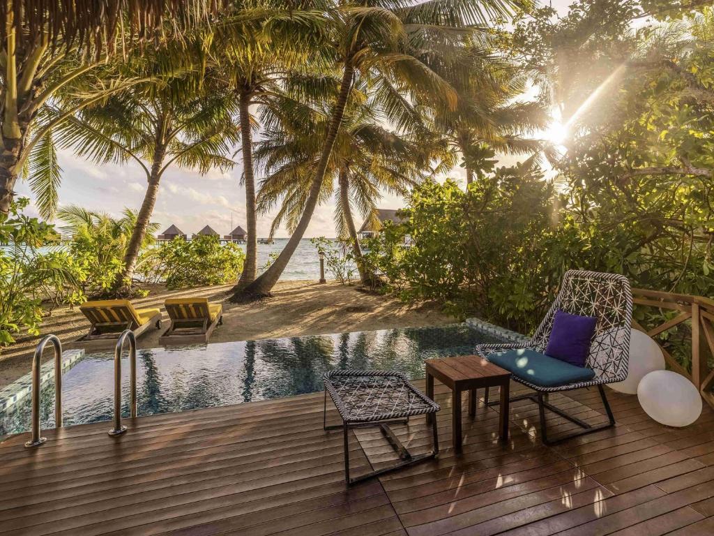 a deck with a chair and a table next to a pool at Mercure Maldives Kooddoo - Adults - Only Escape - 50 percent off Transfers in Gaafu Alifu Atoll