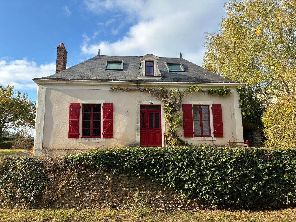 a white house with red windows and a hedge at La Maison du Clocher in Jupilles