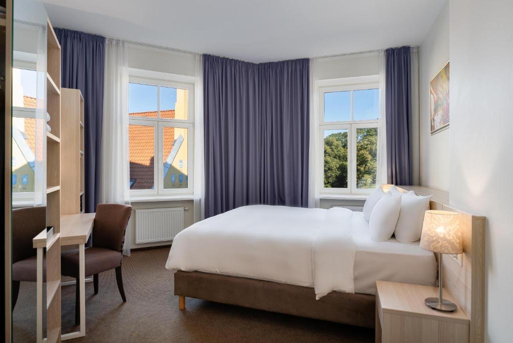 a bedroom with a bed and a desk and two windows at Radisson Hotel Old Town Riga in Rīga