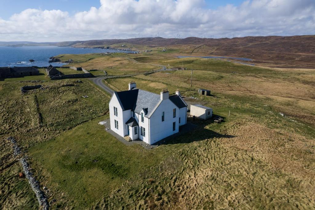 una vista aérea de una casa blanca en un campo en Neap, Shetland Islands, 