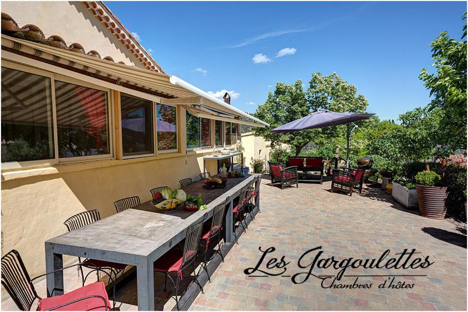 een patio met een tafel en stoelen en een parasol bij Les Gargoulettes in Lauris