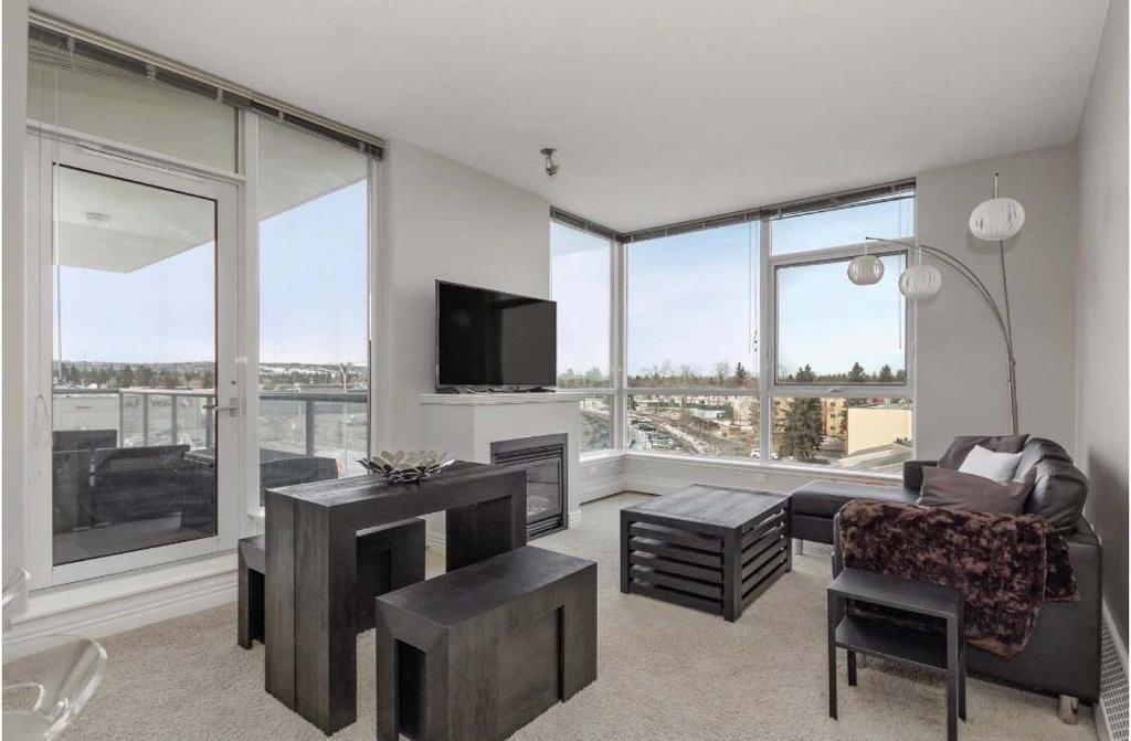 a living room with a couch and a tv and some windows at The Spruce Modern 2BR Condo with Pool & Parking in Calgary