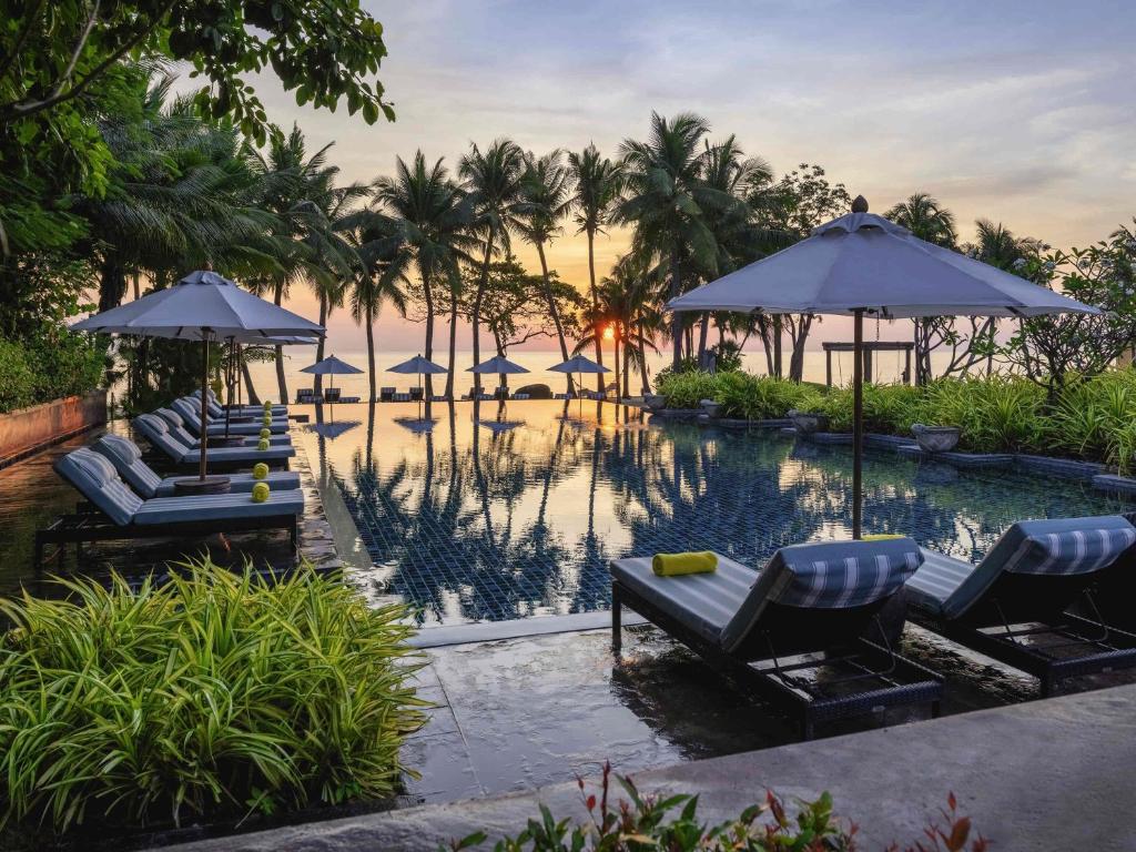 a pool with chairs and umbrellas next to a resort at Mövenpick Asara Resort & Spa Hua Hin in Hua Hin