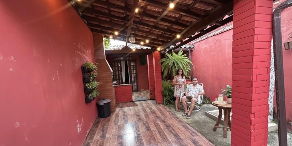 a man and woman sitting on the porch of a red building at Chêles - Casa na Praia do taquari in Paraty