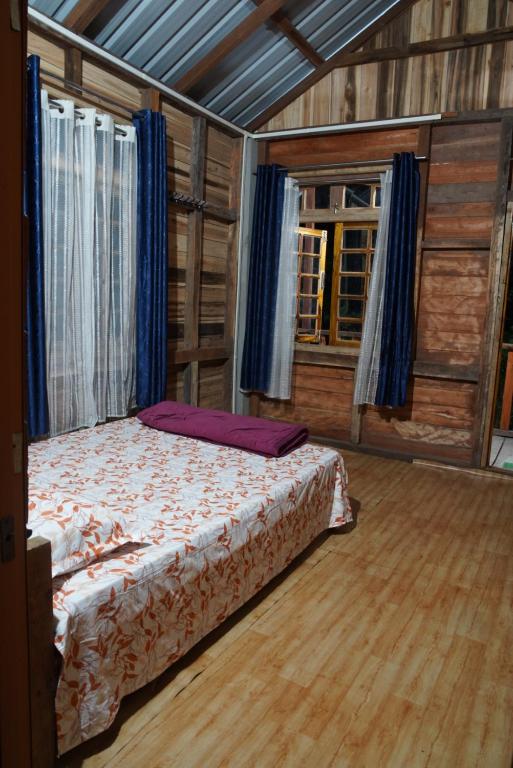 ein Schlafzimmer mit einem Bett in einem Holzzimmer in der Unterkunft Sunset Riverside Cottage, Umngot River in Dawki