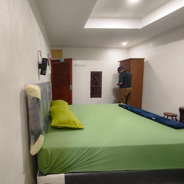 a room with a large bed and a man standing next to it at Loox Hotel Grand Aroya in Mataram