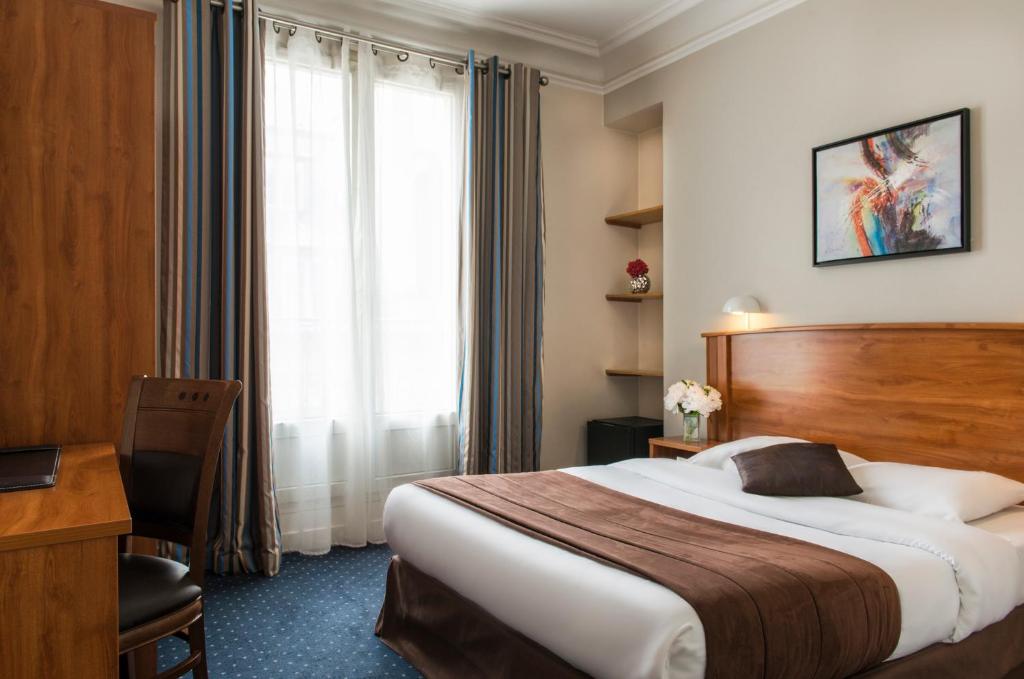 a hotel room with a bed and a desk and a window at Hotel Corona Rodier in Paris