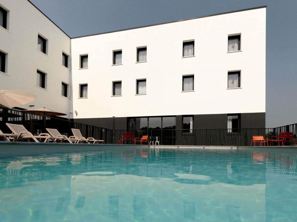a hotel with a swimming pool in front of a building at Greet Hôtel Orthez Bearn in Orthez