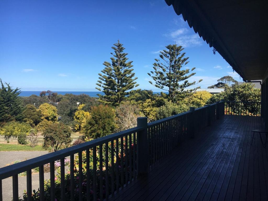 a deck with trees and the ocean in the background at One95 Family Beach House in Anglesea
