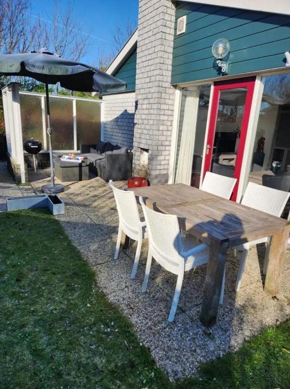 a wooden table with white chairs and an umbrella at Bungalow 002 in Petten