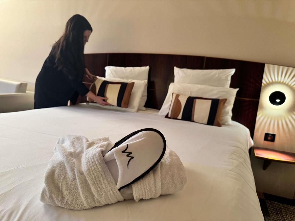 a woman standing next to a bed with a towel on it at Mercure Besancon Parc Micaud - Hotel & Bar in Besançon