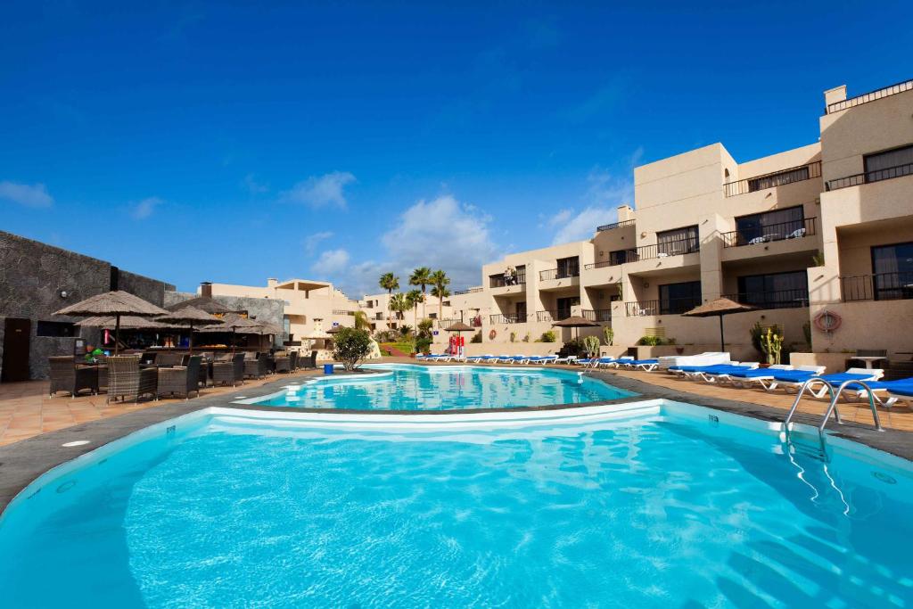 uma grande piscina com água azul em frente aos edifícios em Blue Sea Apartamentos Costa Teguise Gardens em Costa Teguise