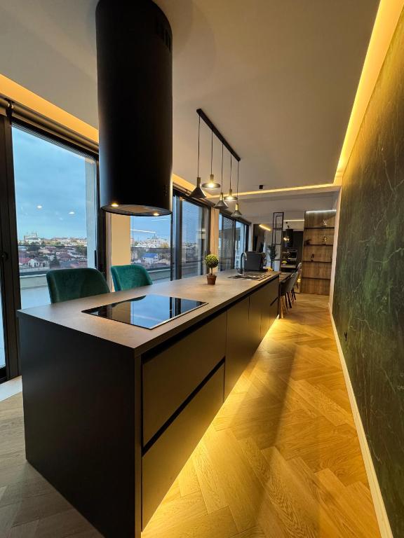 a kitchen with a long counter with chairs and windows at Sky View Penthouse in Craiova