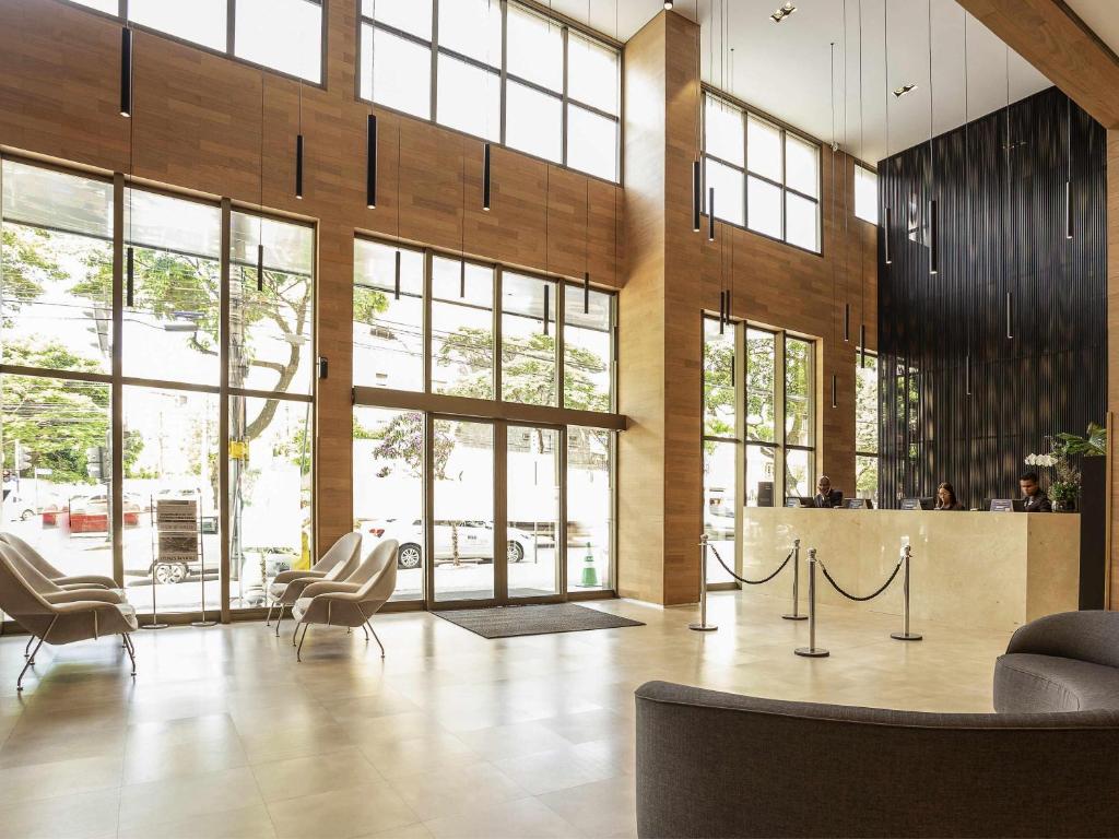 a lobby with chairs and tables and windows at Mercure Belo Horizonte Lourdes in Belo Horizonte