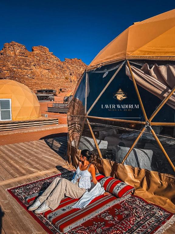 a woman laying on a rug under an umbrella at Laver wadi rum in Wadi Rum