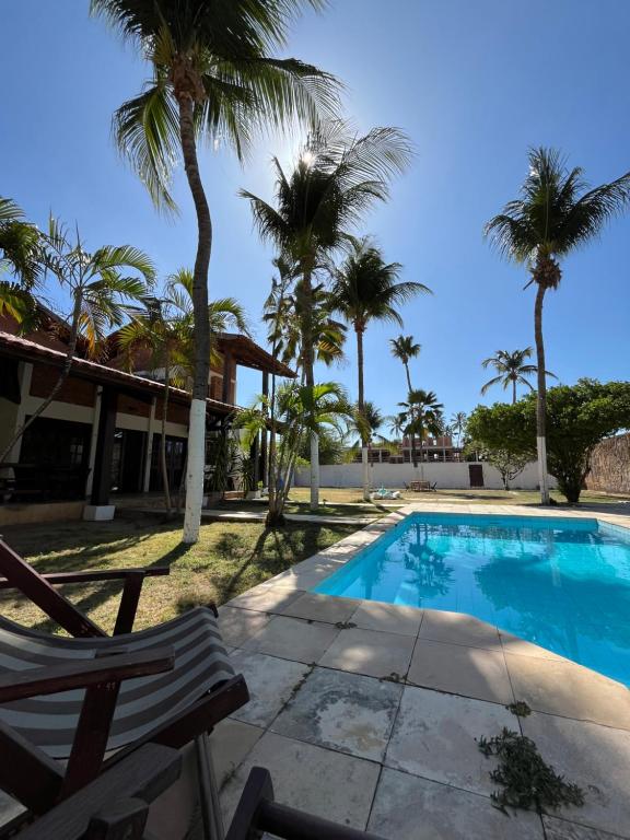 a swimming pool with two chairs and palm trees at Kaza Cumbuco Hostel in Caucaia