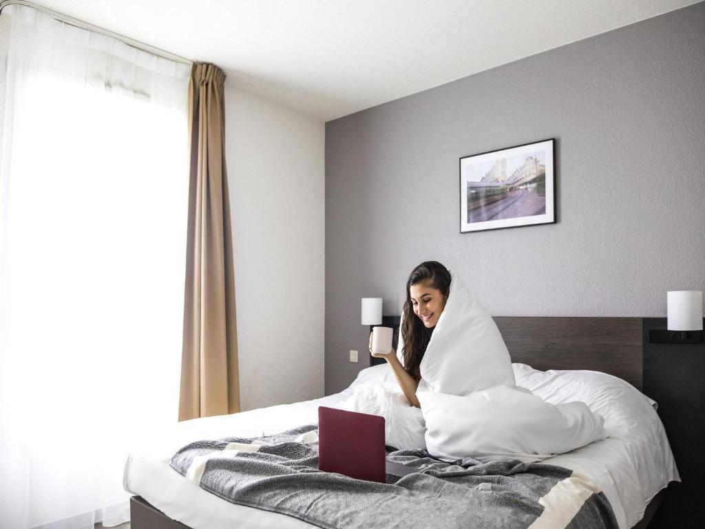a woman sitting on a bed with a laptop at Aparthotel Adagio Access Orléans in Orléans
