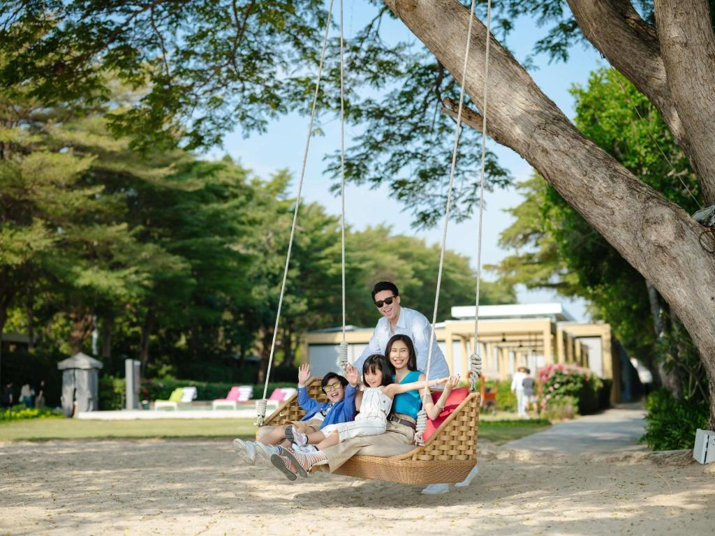 una familia sentada en un columpio bajo un árbol en SO/ Sofitel Hua Hin, en Cha Am