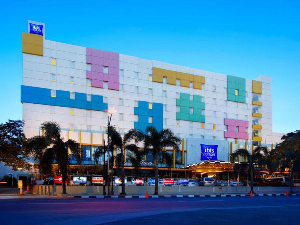 a building with colorful windows and palm trees in front of it at Ibis Budget Jakarta Cikini in Jakarta