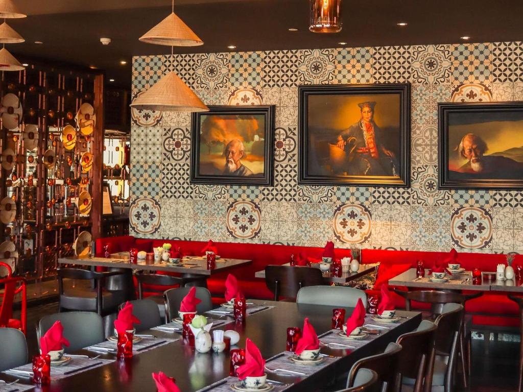 a restaurant with tables and red chairs and portraits on the wall at Hotel Des Arts Saigon Mgallery Collection in Ho Chi Minh City