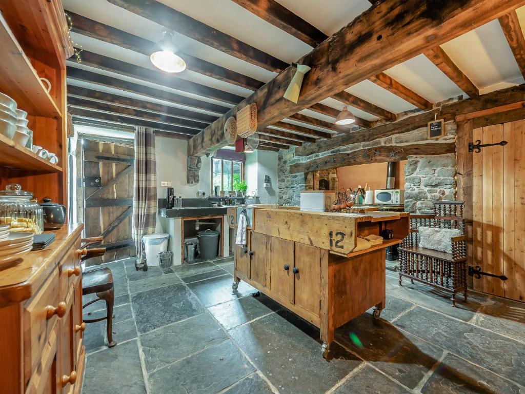 una gran cocina con techos de madera y una pared de piedra. en Ynywsen Dairy Flat, en Llanfynydd