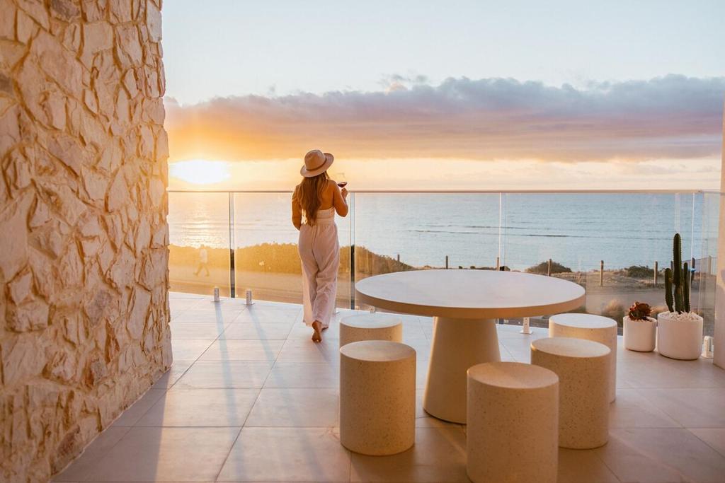 a woman walking on a balcony looking out at the ocean at Sunsets Aldinga Beach, 4 king rooms, rooftop, incredible views in Aldinga Beach