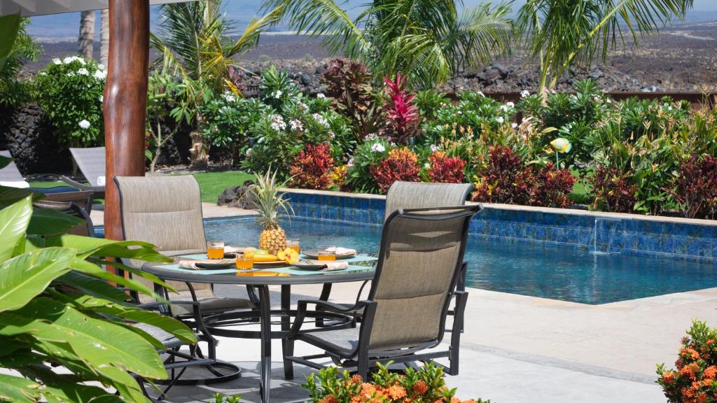 a patio with a table and chairs next to a swimming pool at ISLAND SEABATICAL Restful 3BR Ainamalu Home with Private Pool in Waikoloa