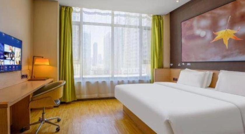 a bedroom with a large white bed and a desk and a window at IU Hotel Taiyuan Changfeng West Street The Mixc in Taiyuan