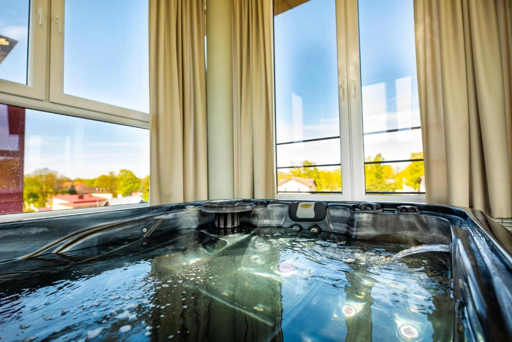 una bañera de hidromasaje en una habitación con ventanas en SPA apartamentai Palanga, en Palanga