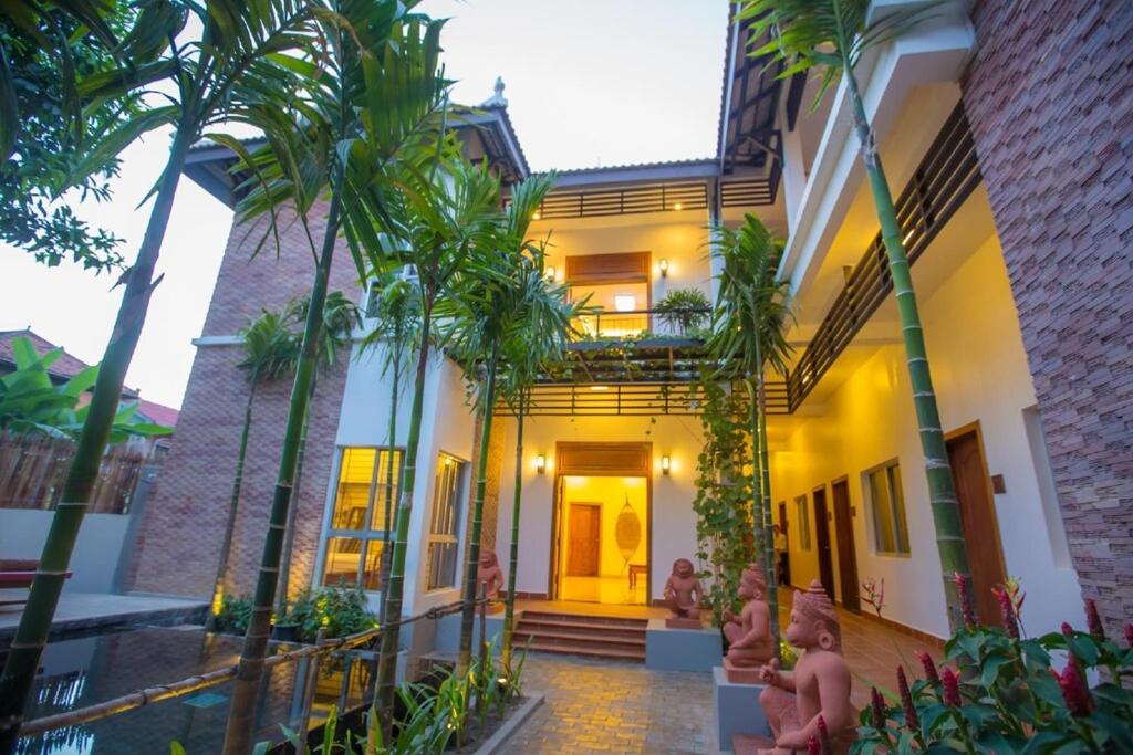 a group of people standing outside of a house with palm trees at La Fontaine de Tara in Siem Reap