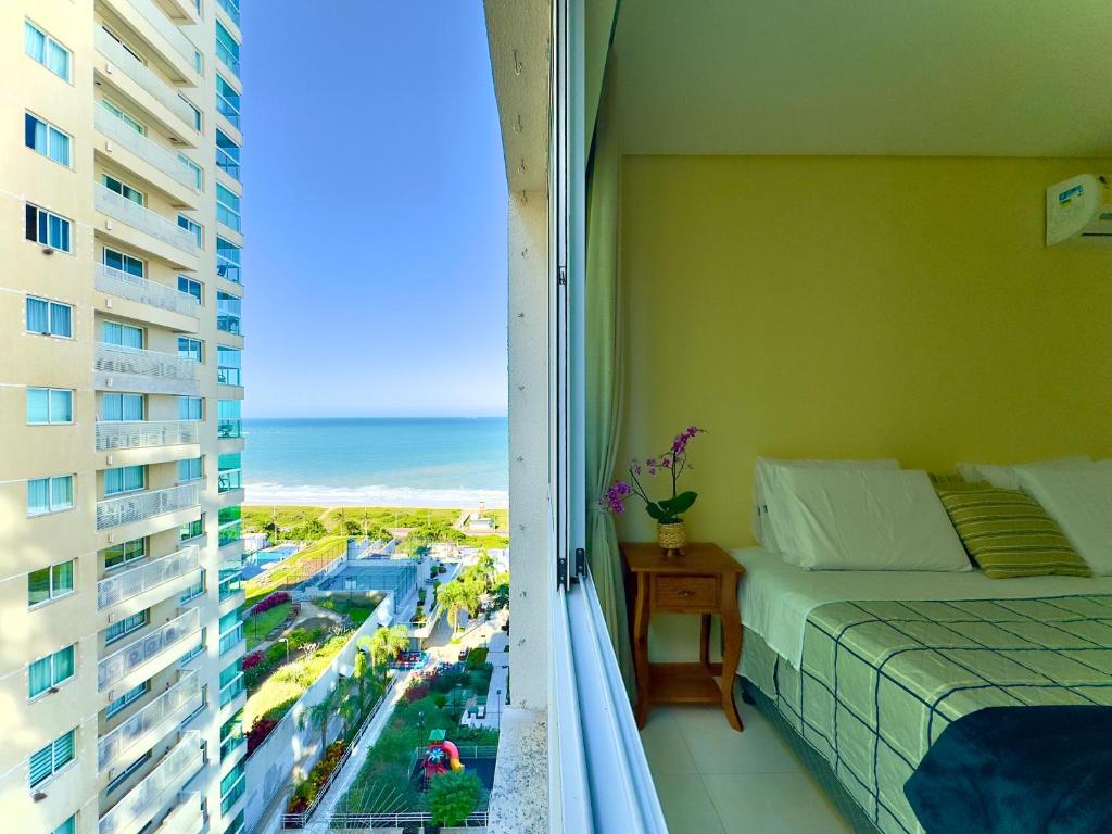 a bedroom with a bed and a balcony with a view of the ocean at Apto Frente Mar Bali Beach Home Club 3 Quartos Climatizados Cozinha Completa Sacada com Churrasqueira 2 Vagas de Garagem Piscina borda infinita Sauna Academia Cinema Quadra Salão de Jogos Pé na Areia 15min do Beto Carrero in Piçarras